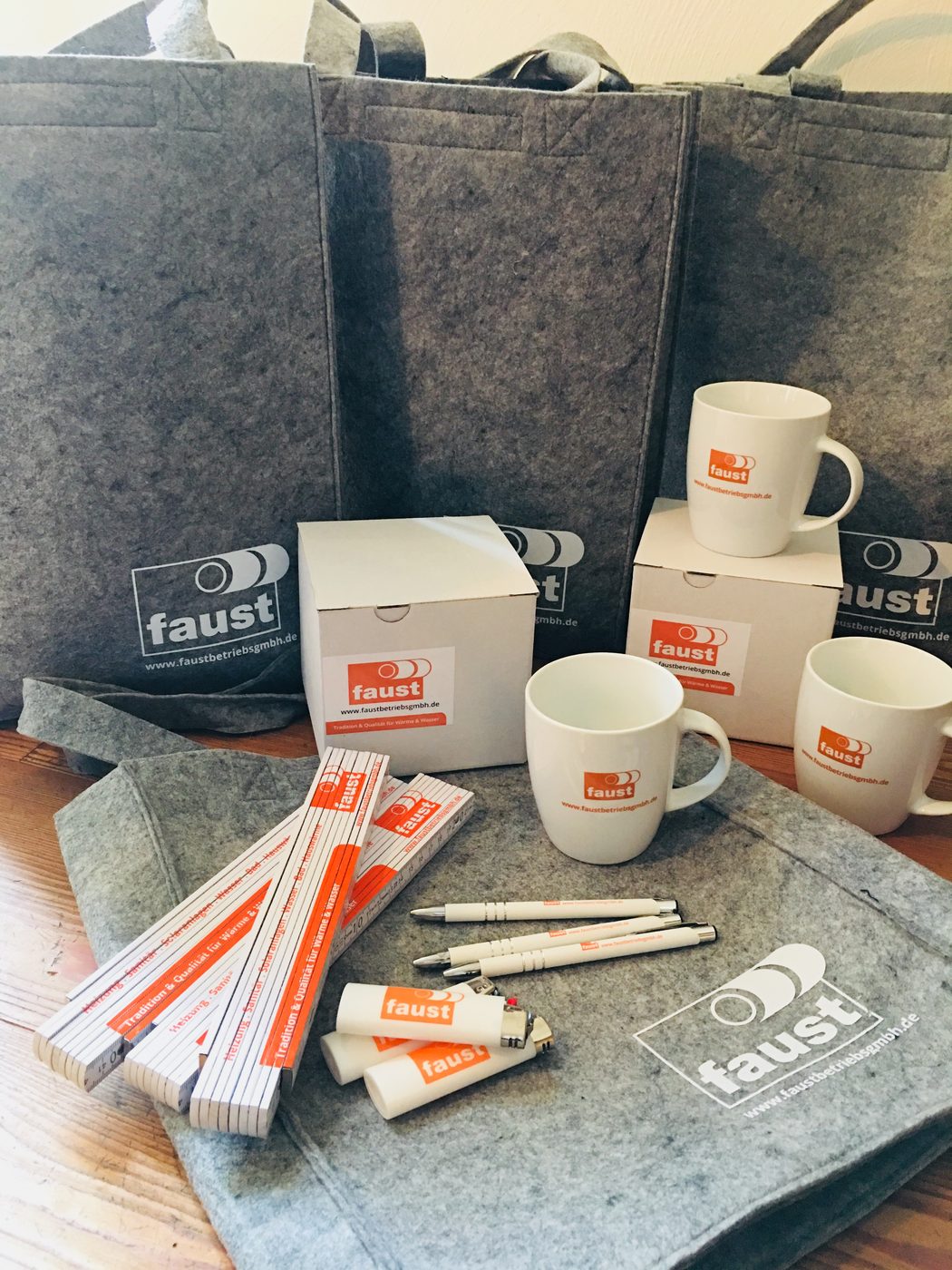 Tassen, Taschen, Zollstöcke und Kugelschreiber im Erscheinungsbild von Faust