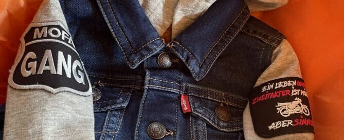 Geburtsgeschenk: kleine Jeansjacke mit Aufnähern in oranger Verpackung
